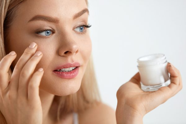 Beauty Woman Face. Closeup Of Beautiful Young Female Model With Fresh Skin Holding Cream Bottle In Hand. Portrait Of Sexy Girl Applying Cosmetic Product Under Eyes. Skincare Concept. High Resolution